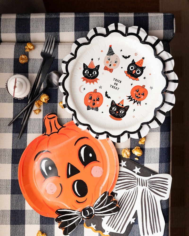 Vintage Halloween tablescape featuring striped scalloped plate as a charger plate, pumpkin shaped plate, black bow napkin, and Halloween icon plate