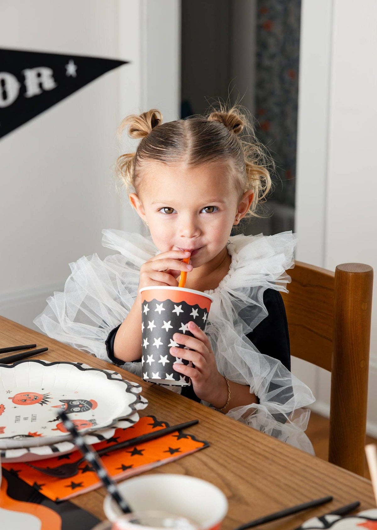 Young girl drinking from a Halloween-themed star party cup at a festive table.