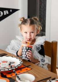 Young girl drinking from a Halloween-themed star party cup at a festive table.