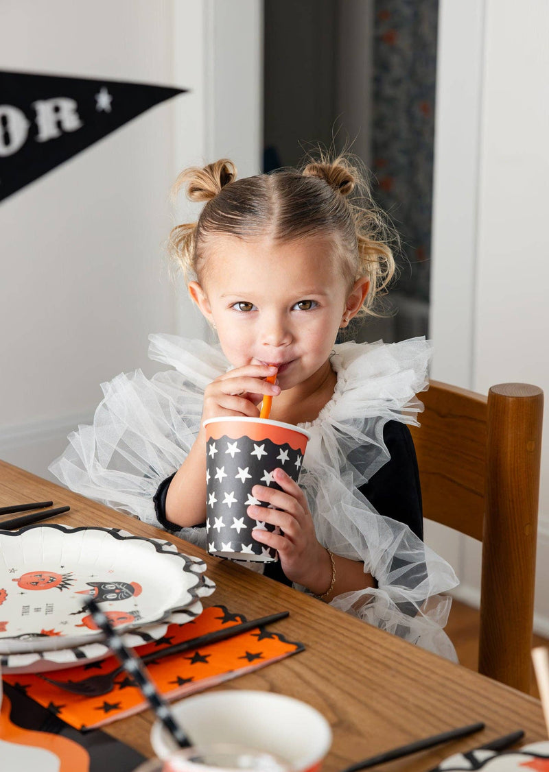 Young girl drinking from a Halloween-themed star party cup at a festive table.