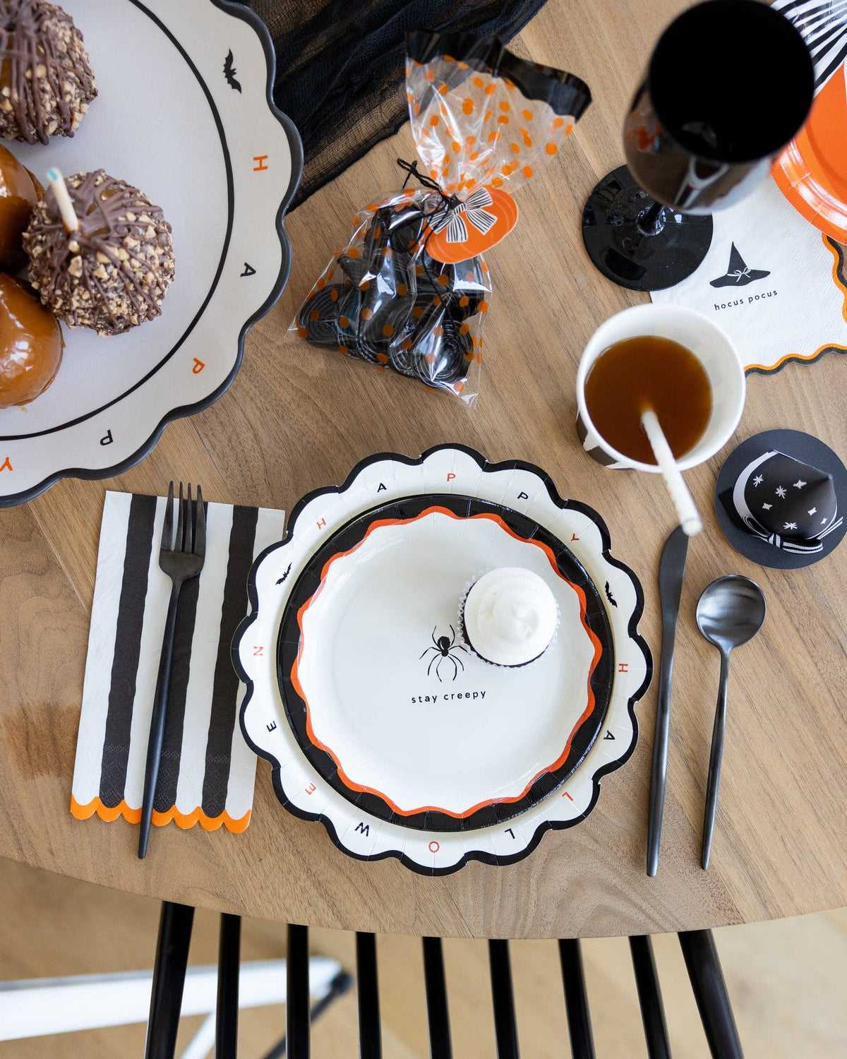 Overhead Halloween table styled shot showing the icon plate layered on the 10" dinner plate on a striped square plate, with HPH cups, treats, and napkins.