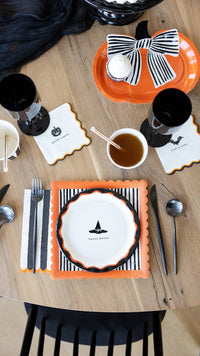 Overhead Halloween table styled shot showing the full HPH layered stack — striped square plate, bow pumpkin plate, and "hocus pocus" icon plate — with cups, cello treat bags, and napkins on a wood table.