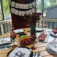 Scalloped Halloween toile paper plates layered under haunted house plates around a round table with a Welcome Witches banner and red flowers