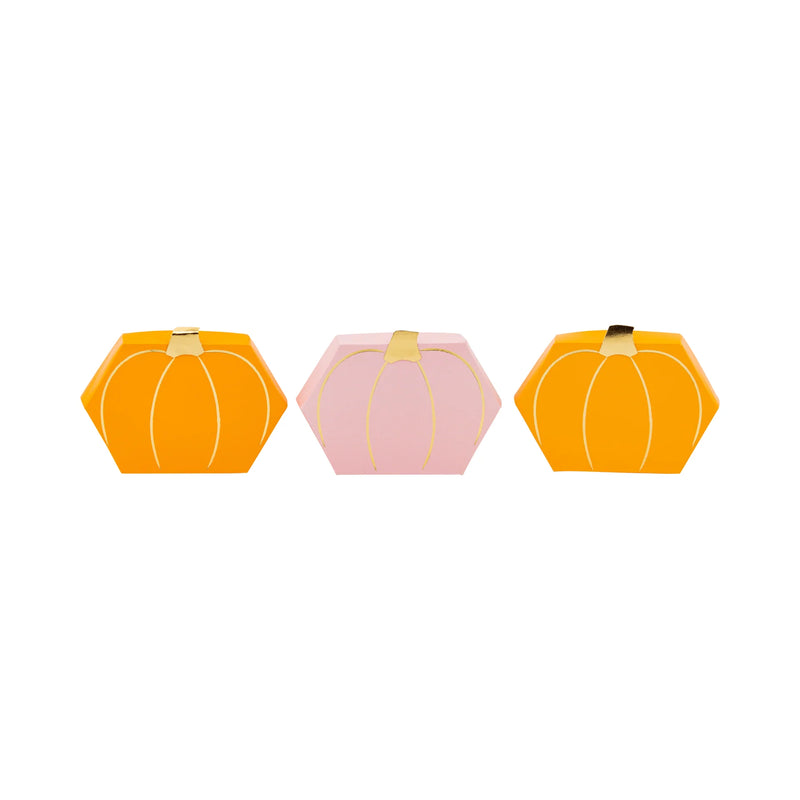 Isolated lineup of three pumpkin favor boxes—bright orange, pastel pink, bright orange—highlighting geometric shape and metallic gold foil accents on each stem.