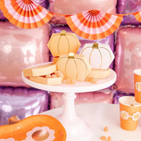 Bright party tablescape with pumpkin favor boxes, orange sunglasses plate, matching cups and scalloped napkins in front of pink and purple balloon wall backdrop.