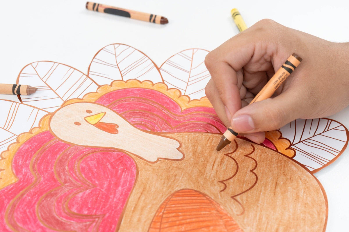 A hand coloring in the turkey coloring placemat with an orange marker, showing the activity in progress.