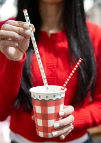 A hand holding a gingham gingham cup with a red-striped straw.