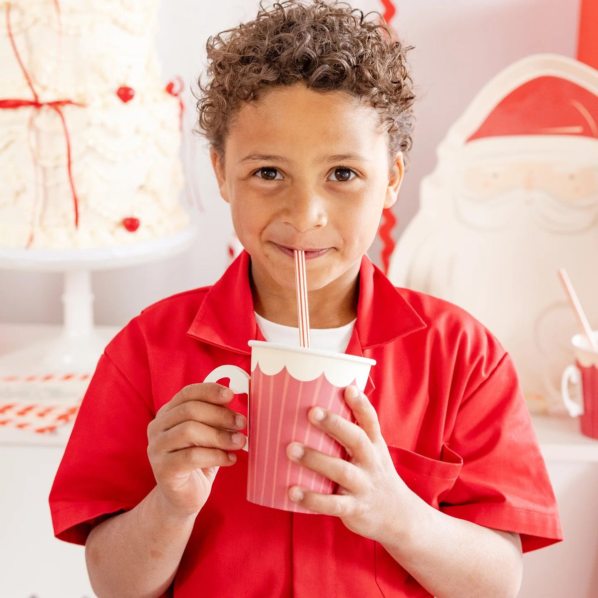 Young boy smiling and drinking from a striped handled Christmas coffee cup disposable at a party.	