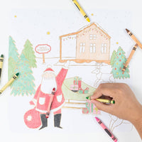Wide shot showing hands coloring the winter village scene with crayons and markers.