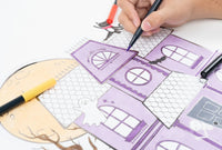 Hands using a purple marker to color in the roof details of the haunted house paper placemat.