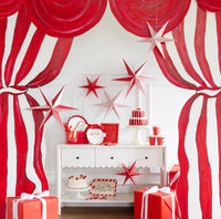Styled room with red and white hanging paper stars over a console against a striped curtain backdrop.