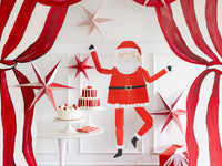 The jointed Santa hanging on a red-and-white striped backdrop beside 3D paper stars above a dessert table.