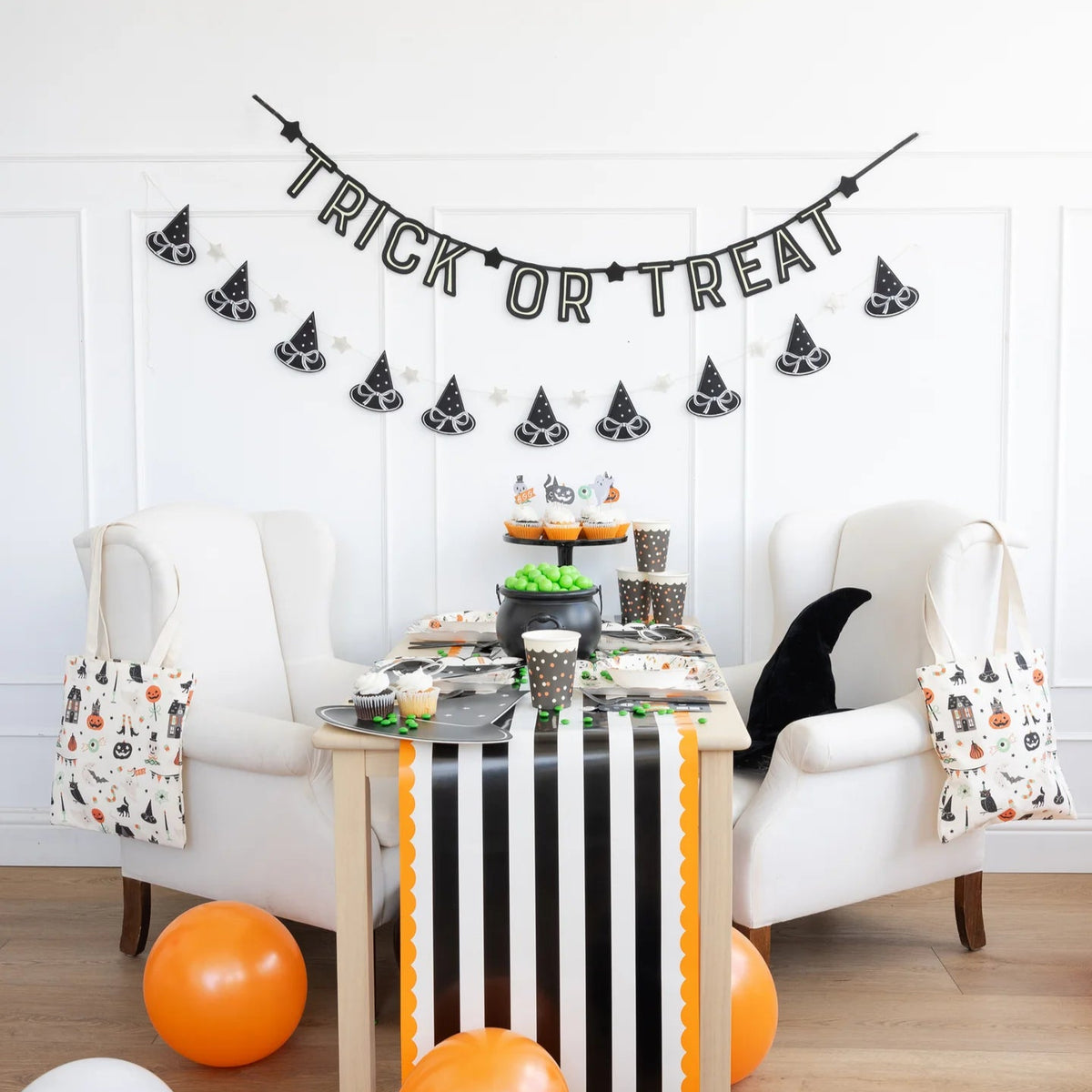 Full-height scene of a striped table runner with balloons and the witch-hat felt banner draped on the wall.
