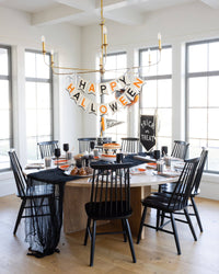Dining room with Halloween decorations, including a 'Happy Halloween' banner and black chairs.