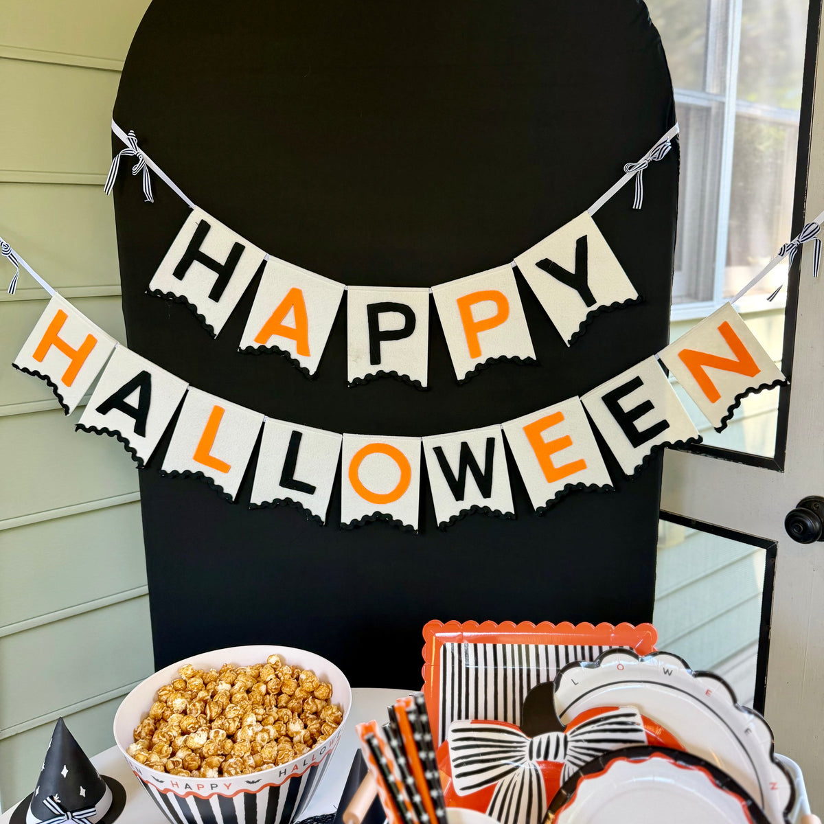 Cream felt Happy Halloween banner with black and orange letters and black rickrack trim, hung on a black arch backdrop
