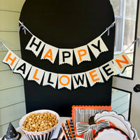 Cream felt Happy Halloween banner with black and orange letters and black rickrack trim, hung on a black arch backdrop