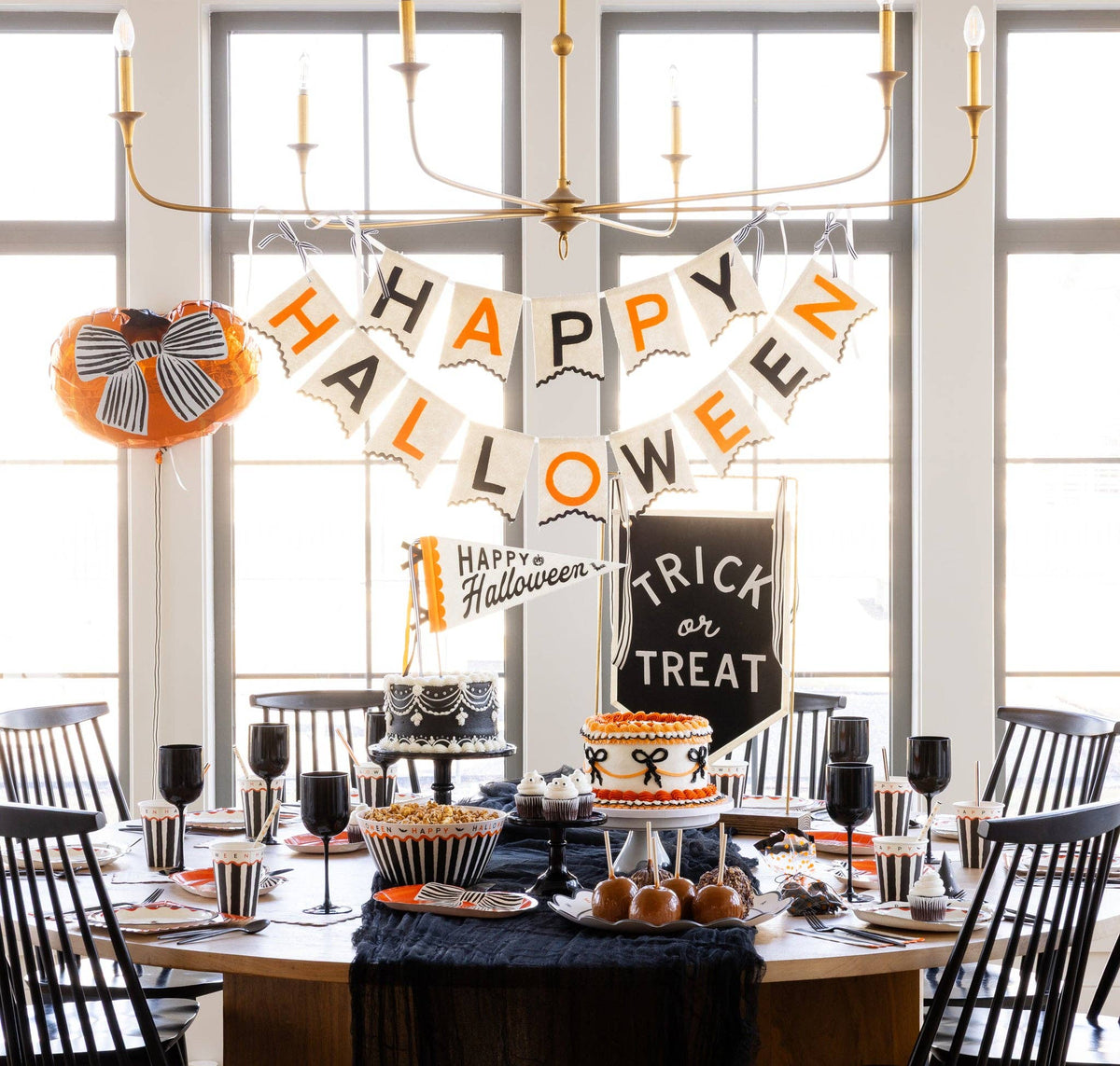 Close-up Halloween dessert table with the Happy Halloween felt banner above a Trick or Treat sign, two cakes, caramel apples, and striped treat cups.