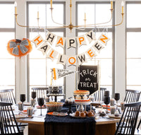 Close-up Halloween dessert table with the Happy Halloween felt banner above a Trick or Treat sign, two cakes, caramel apples, and striped treat cups.