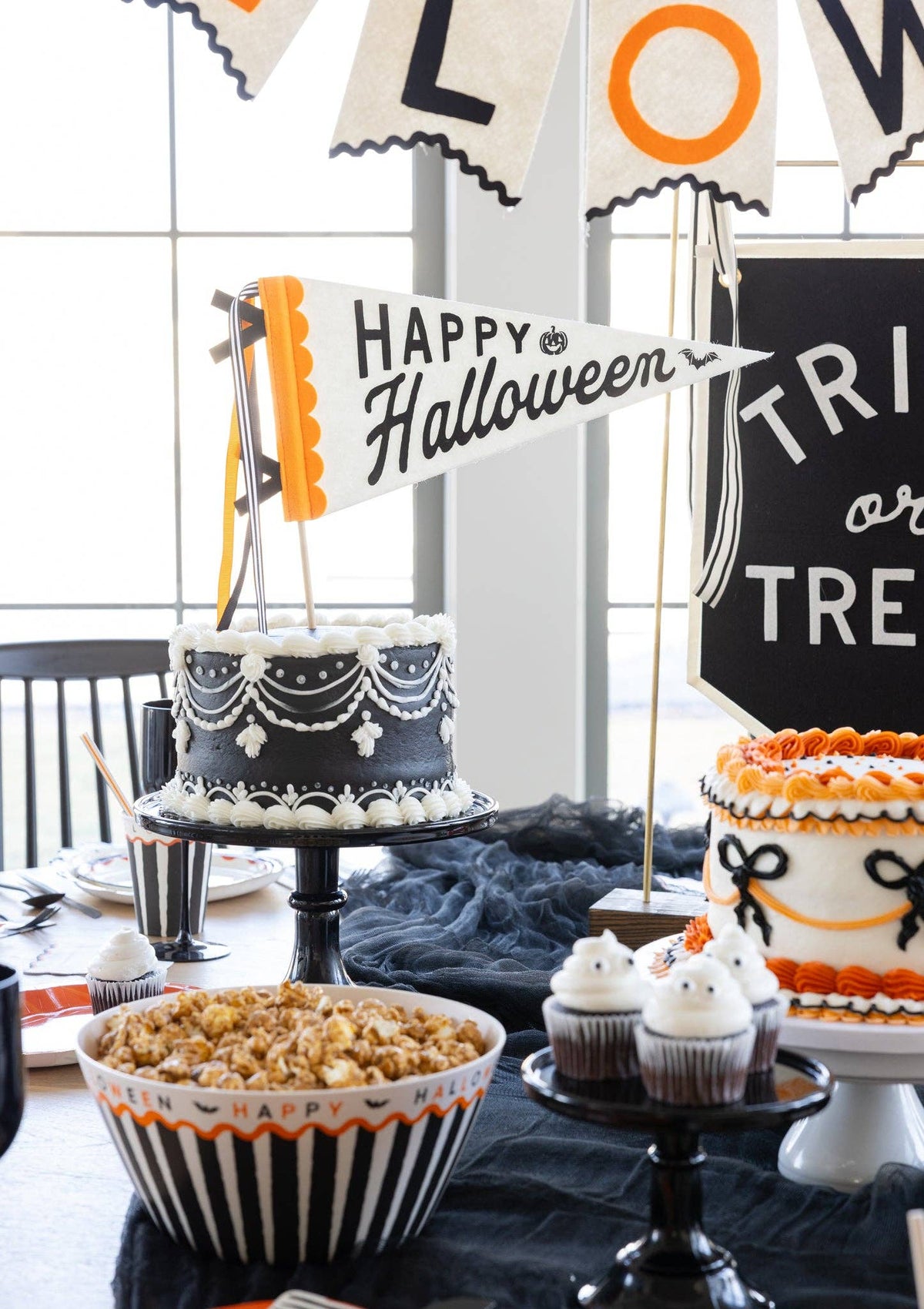 Happy Halloween felt pennant used as a cake topper in a black buttercream Halloween cake, with the Happy Halloween felt banner and a striped popcorn bowl behind it.