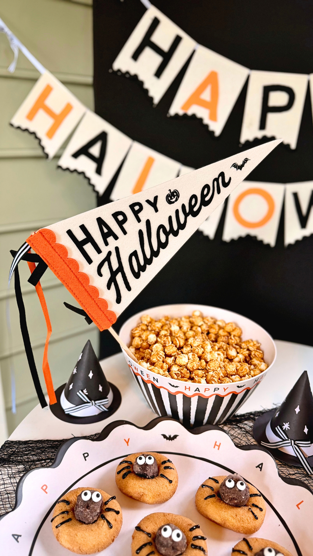 Cream felt Happy Halloween pennant with black script lettering, an orange scalloped edge, and striped ribbon ties, displayed in a bowl of caramel popcorn