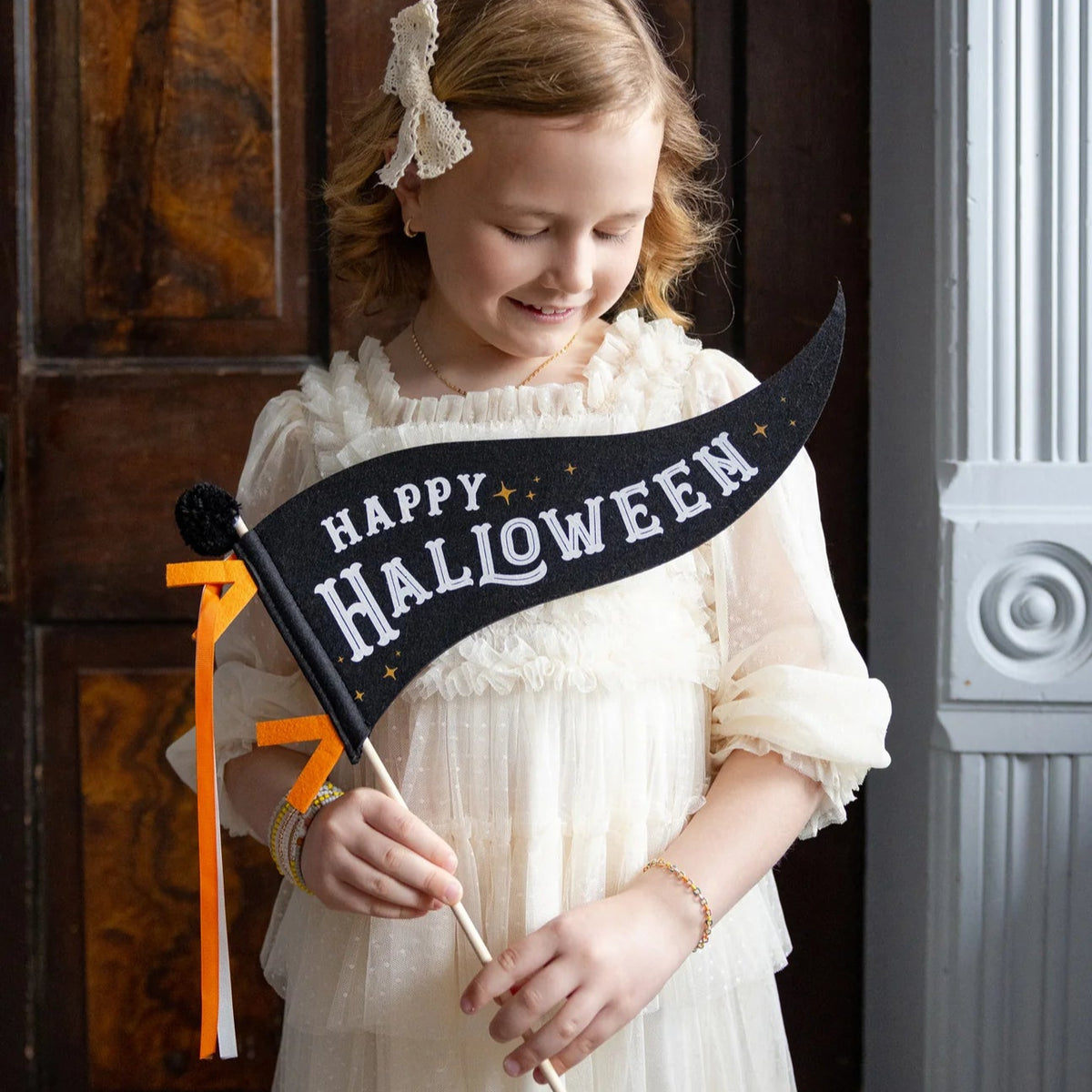 Child holding black Happy Halloween pennant flag on wood dowel—ideal Halloween photo prop.