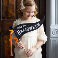 Child holding black Happy Halloween pennant flag on wood dowel—ideal Halloween photo prop.