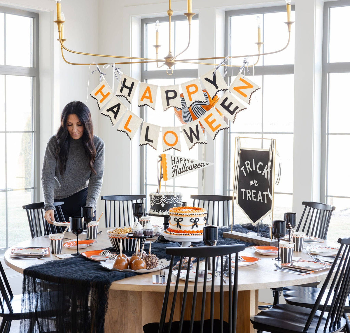 Happy Halloween felt pennant topping a cake on a round Halloween table beneath a Happy Halloween felt banner, with a Trick or Treat sign and black place settings.