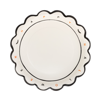 Cream Halloween paper plate with individual "HAPPY HALLOWEEN" letters in black and orange around the rim, tiny bat icons, and a black scalloped edge, overhead flat-lay view.