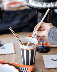 Person holding a Halloween-themed cup with striped design and black and orange straws.
