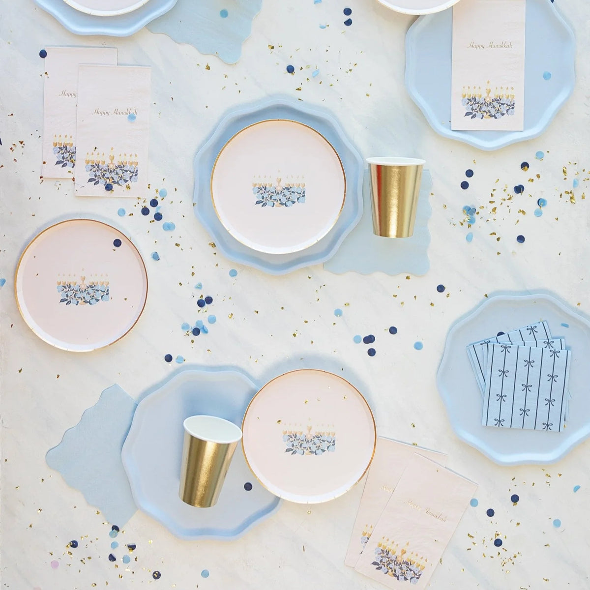 Blush Hanukkah napkins with floral menorah beside light-blue plates and gold cups.