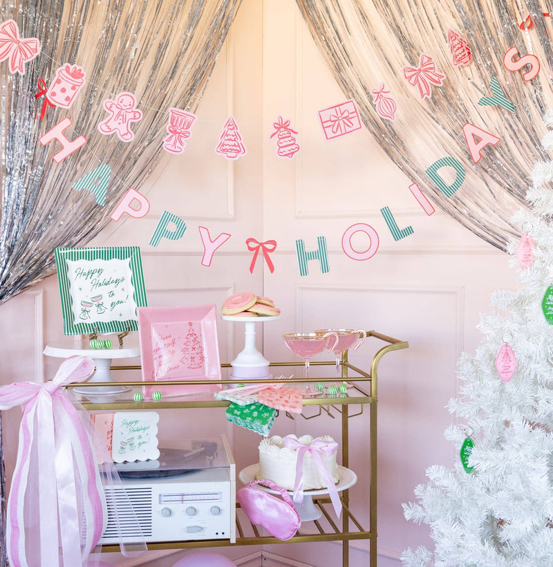 Pink and green Happy Holidays banner styled hanging above a party dessert table
