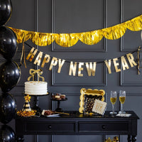 New Year’s Eve dessert table with gold garland, black balloons, and gold party tableware