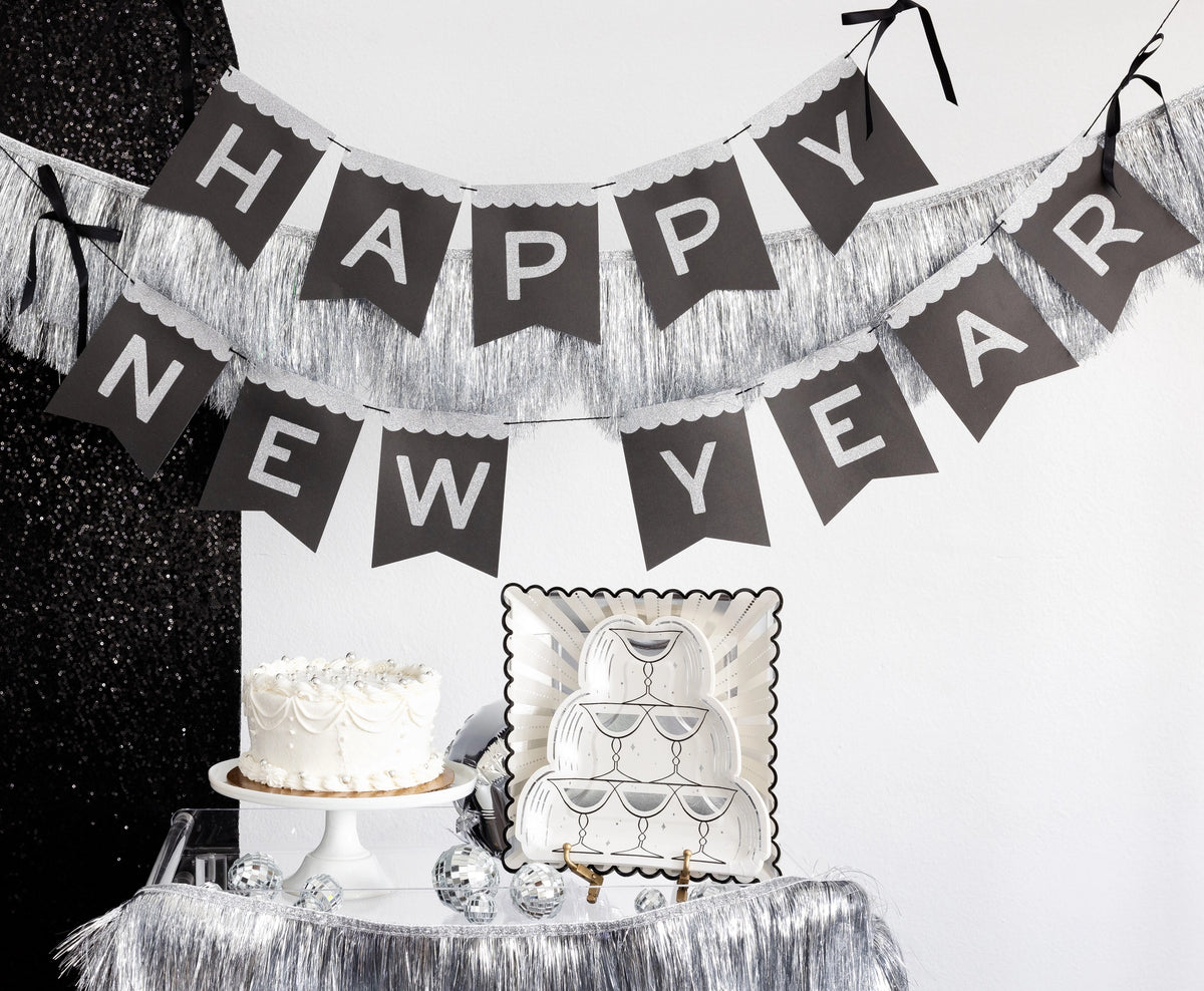 Happy New Year glitter banner hung above a styled dessert table with cake and plates