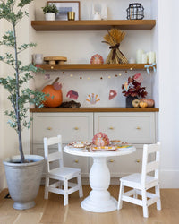 A short area with a white table and chairs, shelves with decorative items, and a potted plant showcasing the banner. 