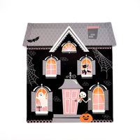 Haunted house Halloween paper plate shaped like a black manor with a grey roof, glowing peach windows, floating ghosts, a black cat, spider webs, and an orange jack-o-lantern by the door on a white background.