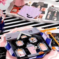 Halloween table setting featuring a black and white striped paper runner layered under haunted house shaped plates and bat napkins.