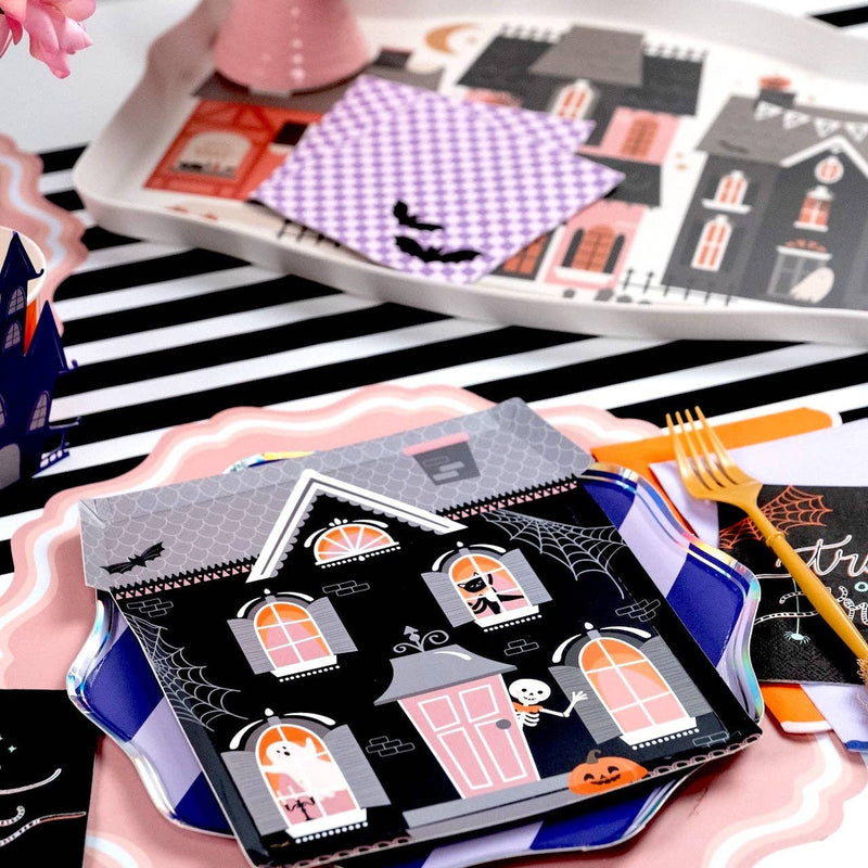 Halloween table setting featuring a black and white striped paper runner layered under haunted house shaped plates and bat napkins.