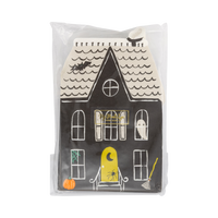 Front of the retail package: the top haunted house napkin face-up with a small gold brand sticker, showing the black mansion with arched white windows, a ghost, a bat, green spiderweb, broom, pumpkin, and yellow crescent-moon door. Straight-on packaging shot.
