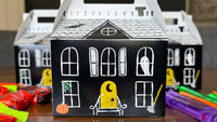 White haunted house paper treat box decorated with black windows, doors, and a ghost, styled as a kids Halloween craft