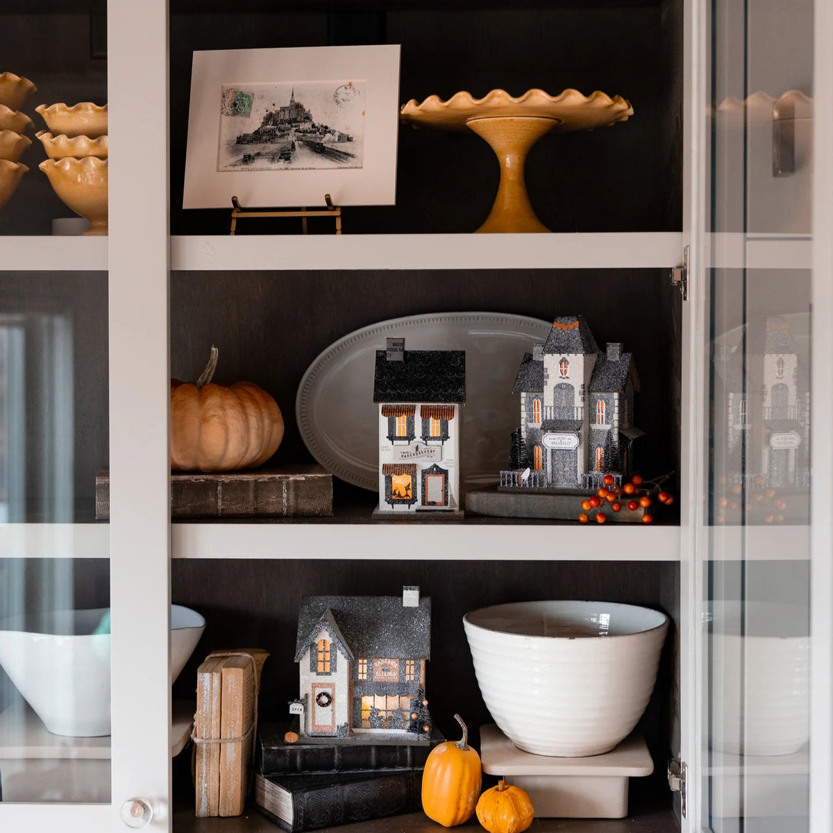 Dead & Breakfast haunted house glowing on a styled cabinet shelf with pumpkins and books—cozy Halloween mantel display.