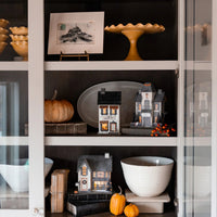 Dead & Breakfast haunted house glowing on a styled cabinet shelf with pumpkins and books—cozy Halloween mantel display.