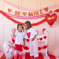 Kids in front of Valentine party setup with triple heart garlands and banners