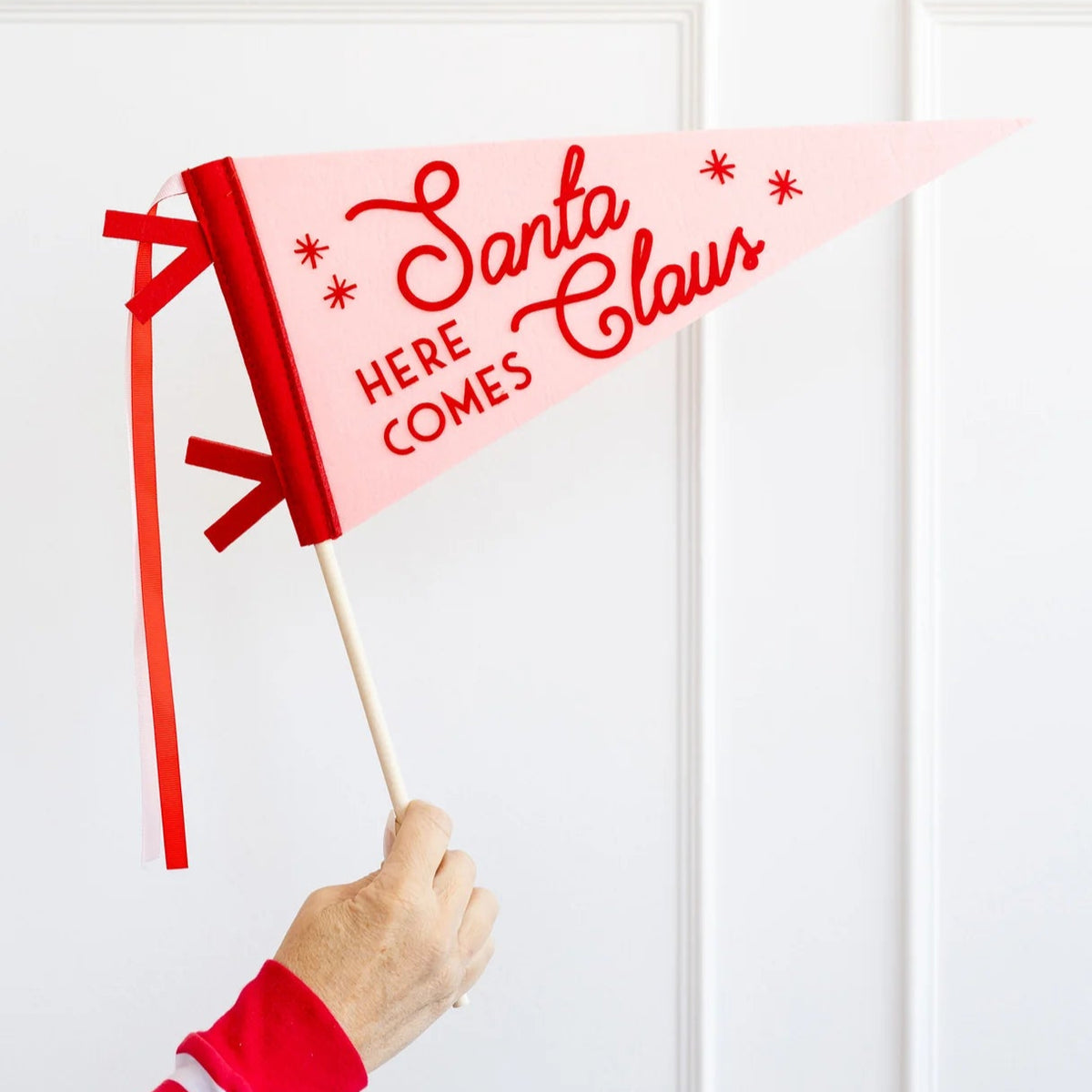 Hand holding Here Comes Santa Claus felt pennant on dowel—fun Christmas photo booth prop.