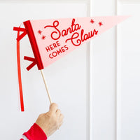 Hand holding Here Comes Santa Claus felt pennant on dowel—fun Christmas photo booth prop.