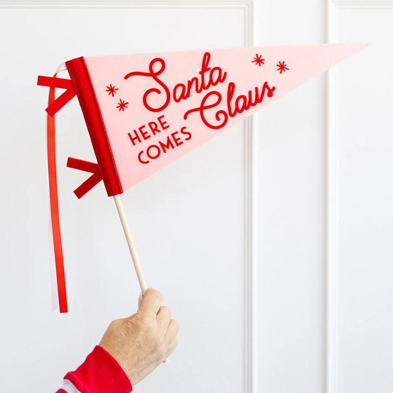 Hand holding Here Comes Santa Claus felt pennant on dowel—fun Christmas photo booth prop.