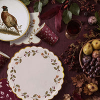 Fall table on burgundy linen with a pheasant plate, berry wreath plate, burgundy leaf cups, and a berry sprig napkin
