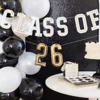 A Class of 2026 Sign hanging as a graduation photo backdrop next to white balloons and a black sequin wall.