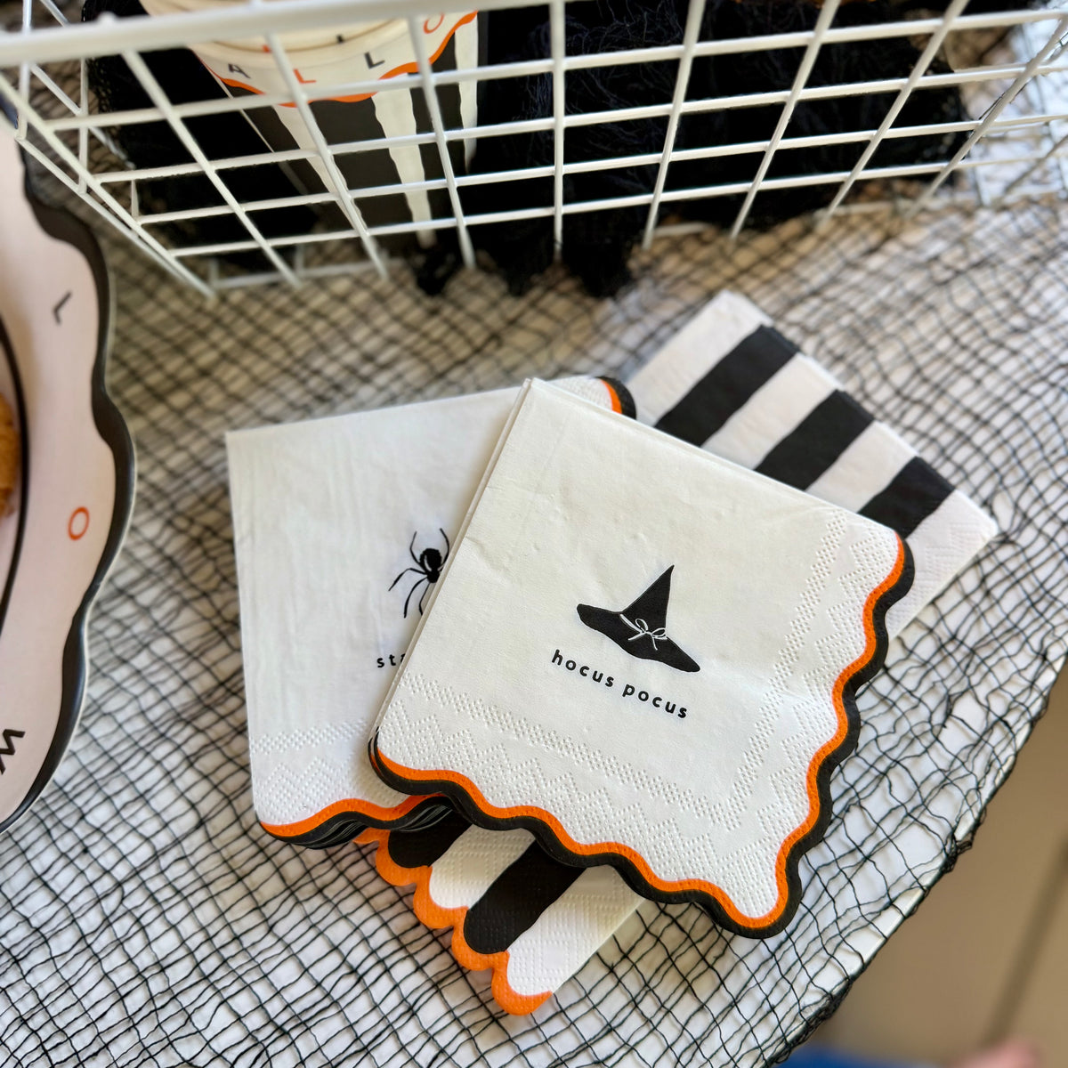 Black and white striped Halloween cocktail napkins with a scalloped orange edge, layered under hocus pocus and stay creepy napkins