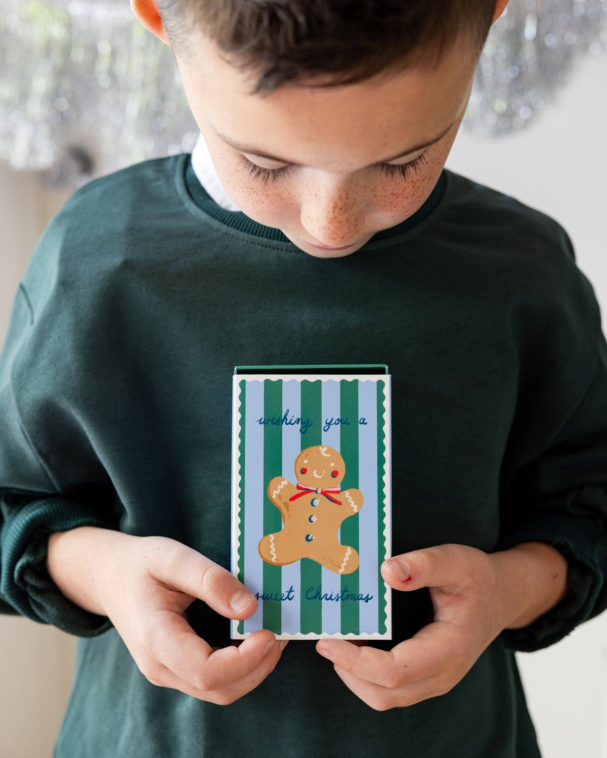 Child holding green Christmas treat box with red holiday house illustration