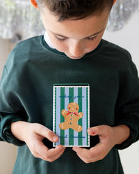 Child holding green Christmas treat box with red holiday house illustration